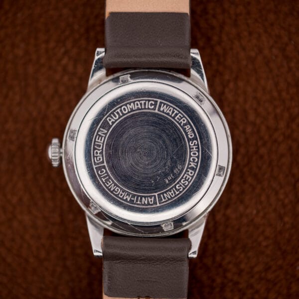 Gruen stainless case back engraved GRUEN AUTOMATIC, WATER AND SHOCK RESISTANT, ANTI-MAGNETIC around an engine-turned center.