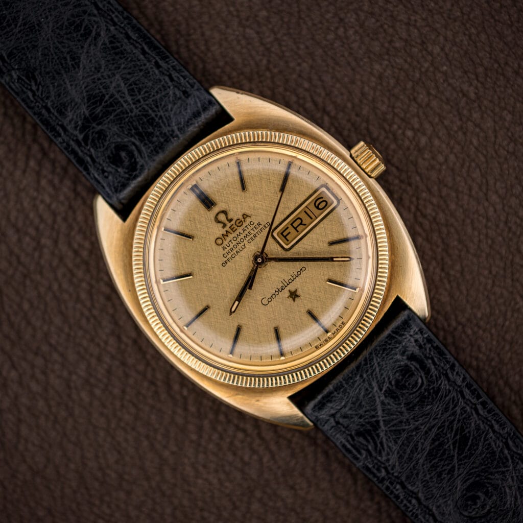 Vintage Omega Constellation with champagne gold linen dial, day-date window, and fluted gold-capped bezel on black ostrich strap.