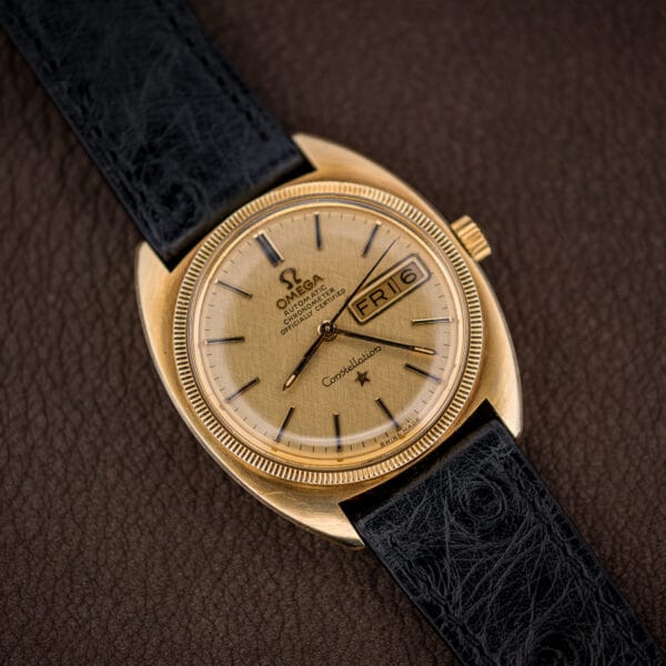 Vintage Omega Constellation day-date on black ostrich strap, showing the gold linen dial and stepped cushion case profile.