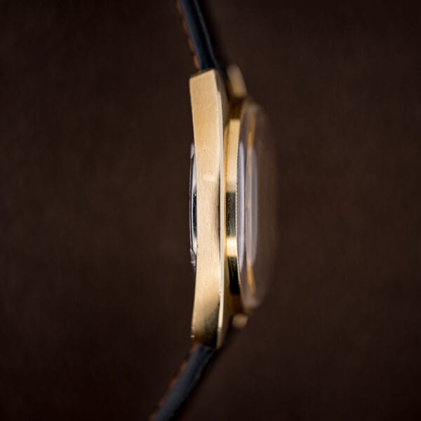 Side profile of the gold-capped cushion case and downturned lug, with the black ostrich strap curving away.