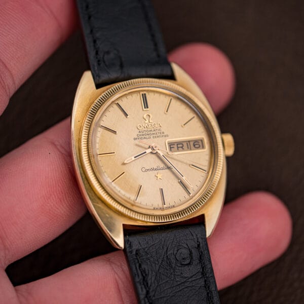 Vintage Omega Constellation held in hand, the gold cushion case and day-date dial catching natural daylight.