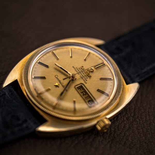Three-quarter Omega Constellation showing the day-date aperture, faceted hour markers, and the warm champagne tone of the linen dial.