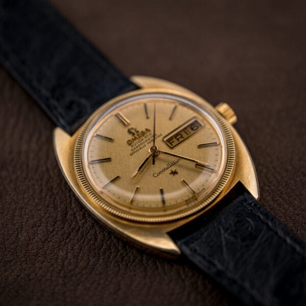 Gold Omega Constellation against a dark ground, its linen dial, star emblem, and day-date display clearly legible.