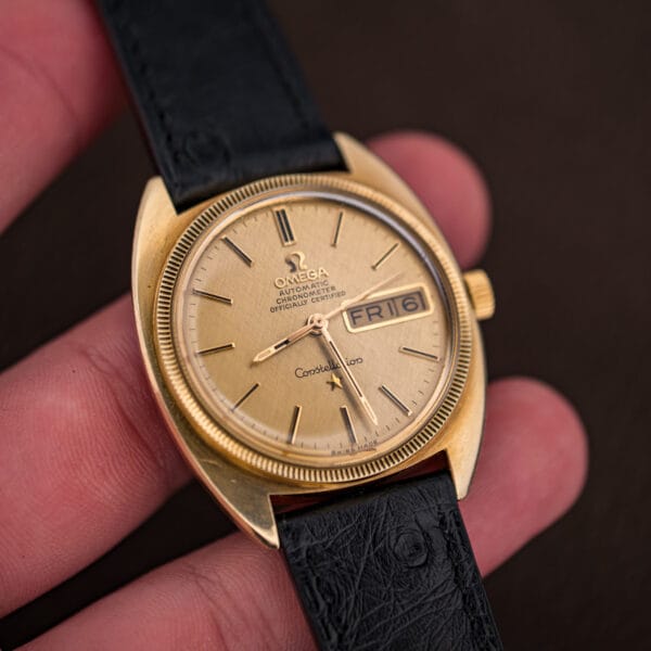 Gold Omega Constellation in hand under warm light, the linen dial, star emblem, and day-date window in focus.