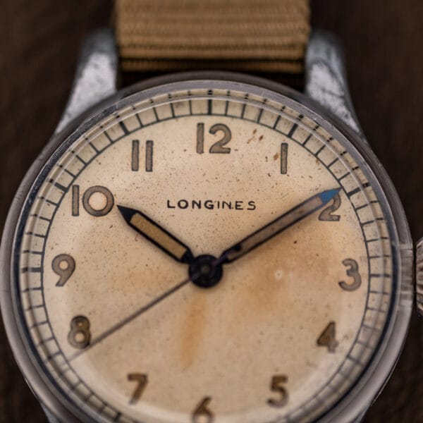 Longines 12L cream dial close-up, aged radium-era numerals and cathedral hands over heavy foxing patina