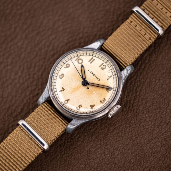 Vintage Longines field watch dial at an angle, blued sweep seconds hand and fluted crown at three o'clock