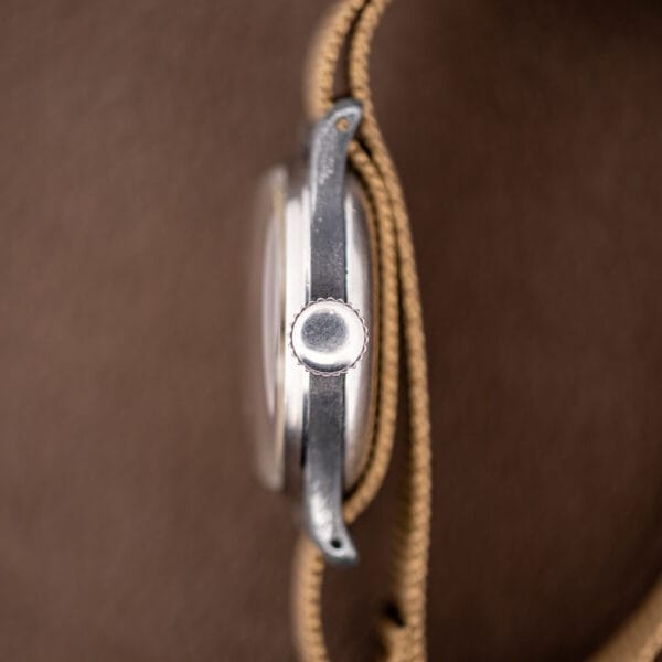 Vintage Longines field watch side profile, worn base-metal case flank and fluted winding crown