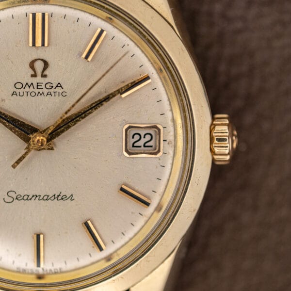 Faceted gold date frame at three on the Omega 166.010, beside the fluted Omega signed crown