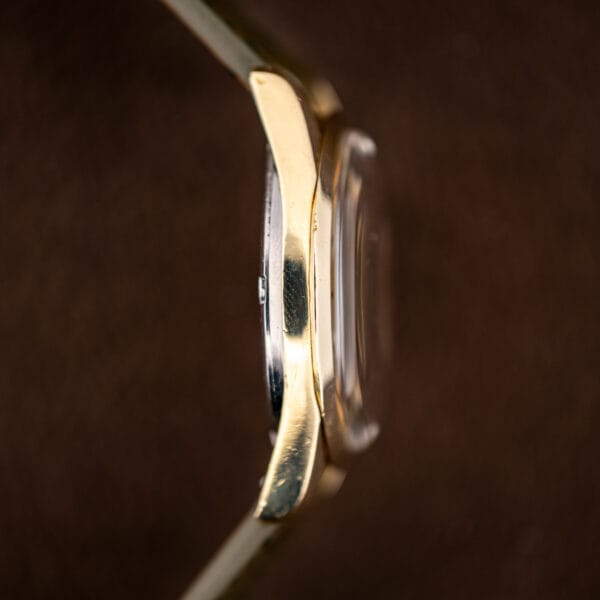 Side profile of the Omega 166.010 showing gold capped bezel and lugs over a stainless steel caseback