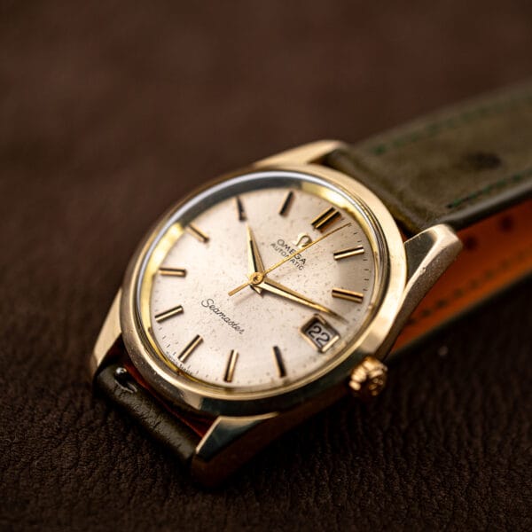 Tilted view of the 166.010 with the tan underside of the olive ostrich strap visible beside the gold capped case