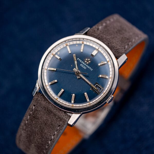Three-quarter hero of the Eterna-Matic 1000, blue sunburst dial, five-dot logo and grey suede strap.