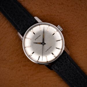 Vintage Eterna Vision 132 T dress watch face-up on tan leather, silver sunburst dial and black strap.