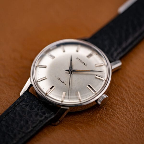Tilted view of the round stainless case and signed fluted crown at three o'clock, dial catching light.