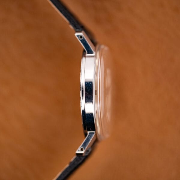 Profile of the faceted, drilled lugs and polished case flank on the tan leather backdrop.