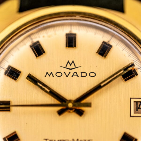 Macro of Movado M chevron logo and applied gold baton markers on champagne Tempomatic dial