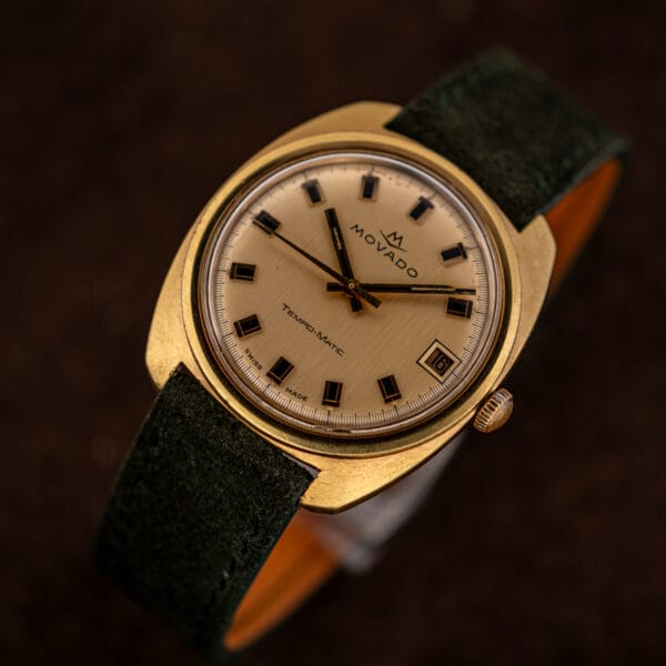 Angled shot on forest green suede, champagne linen dial catching light across the applied batons