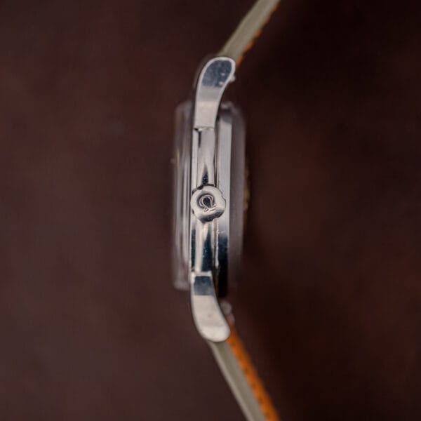 Omega-signed crown on the Constellation 2943-2, case flank in profile against the olive ostrich strap
