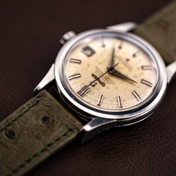 Raking light across the aged off-white Constellation dial, speckled patina and stepped date aperture in relief
