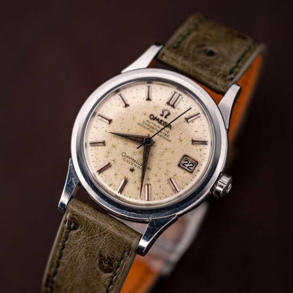 Vintage Omega Constellation Calendar chronometer angled on olive ostrich, date window reading twenty-two at three