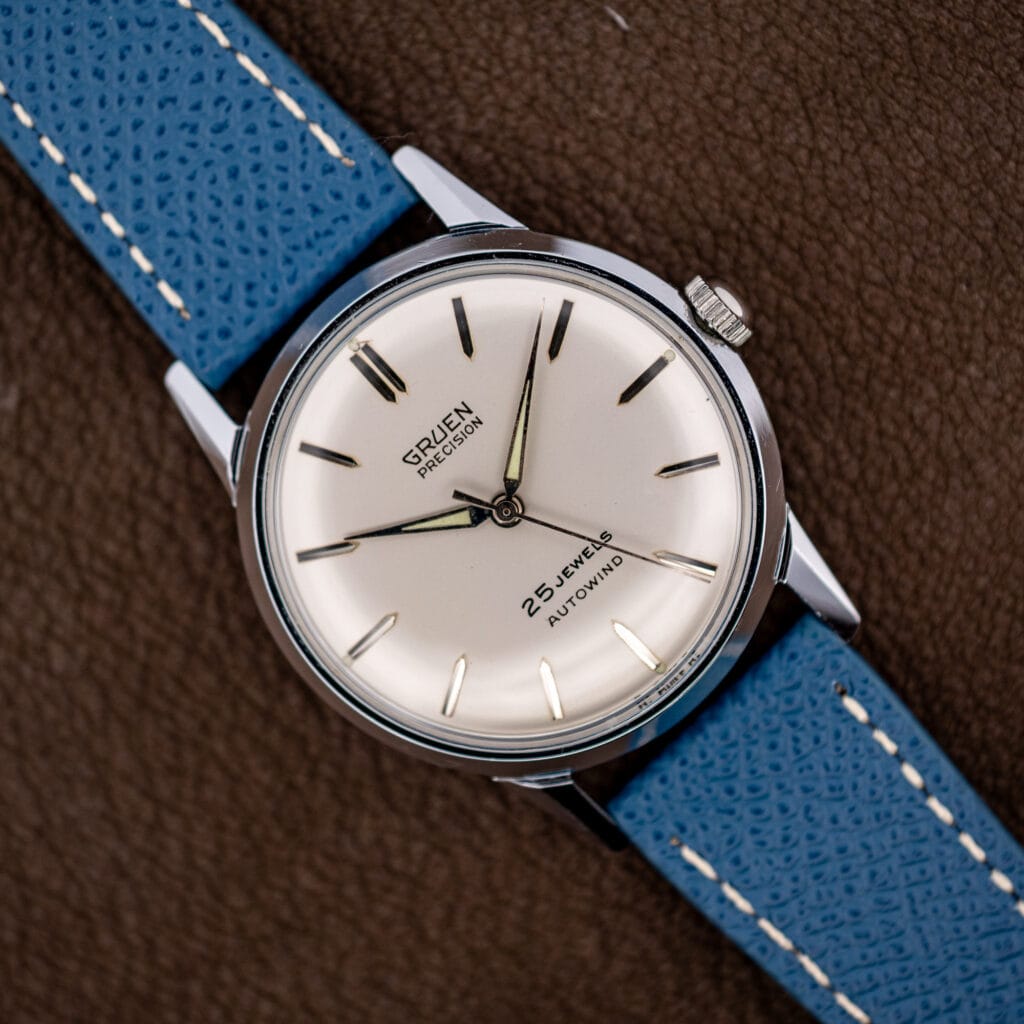 Vintage Gruen Precision Autowind with a silvered white dial on a blue leather strap, shown face-up.