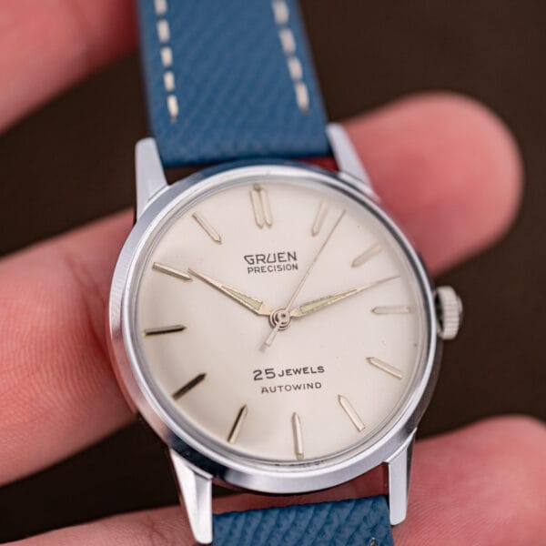 Vintage Gruen Precision Autowind held in hand, silvered dial and blue leather strap in natural light.