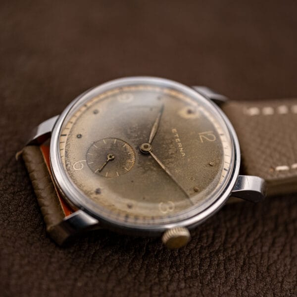Vintage Eterna dial at an angle, small seconds at six and fluted gold-tone crown against taupe leather strap