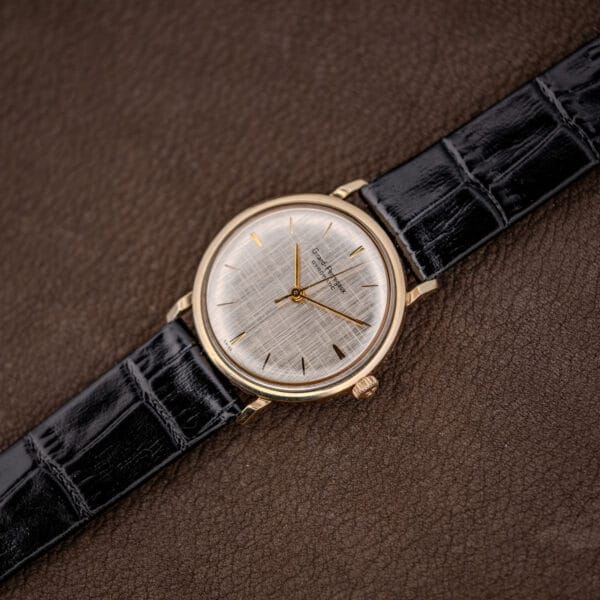 Vintage Girard Perregaux Gyromatic watch angled on brown leather with its black crocodile-grain strap laid out flat