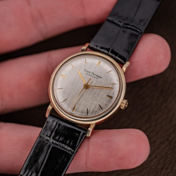Girard Perregaux Gyromatic held at an angle, applied gold hour batons catching light across the linen dial