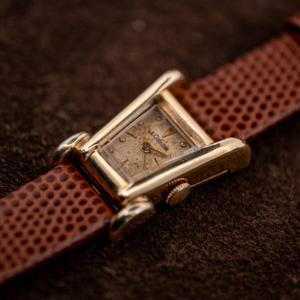 Angled view of the LeCoultre Aristocrat dial and crown, gold markers catching light against tan patina.