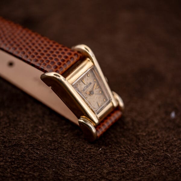 LeCoultre Aristocrat tilted to show the sculptural flared lugs and tapered dial, gold filled case and tan dial.