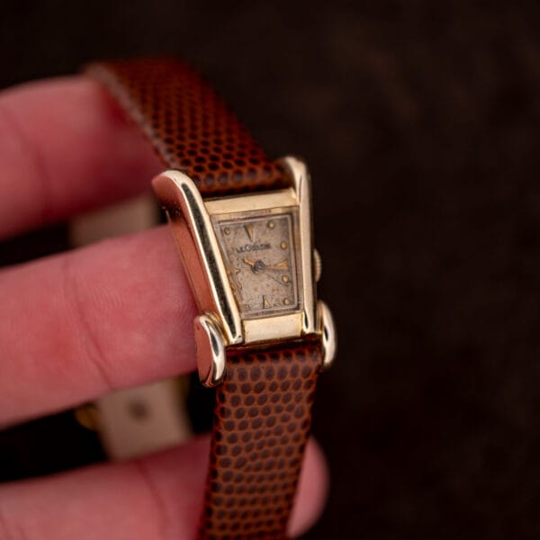 LeCoultre Aristocrat held in hand for scale, gold filled asymmetric case and warm tan patinated dial.