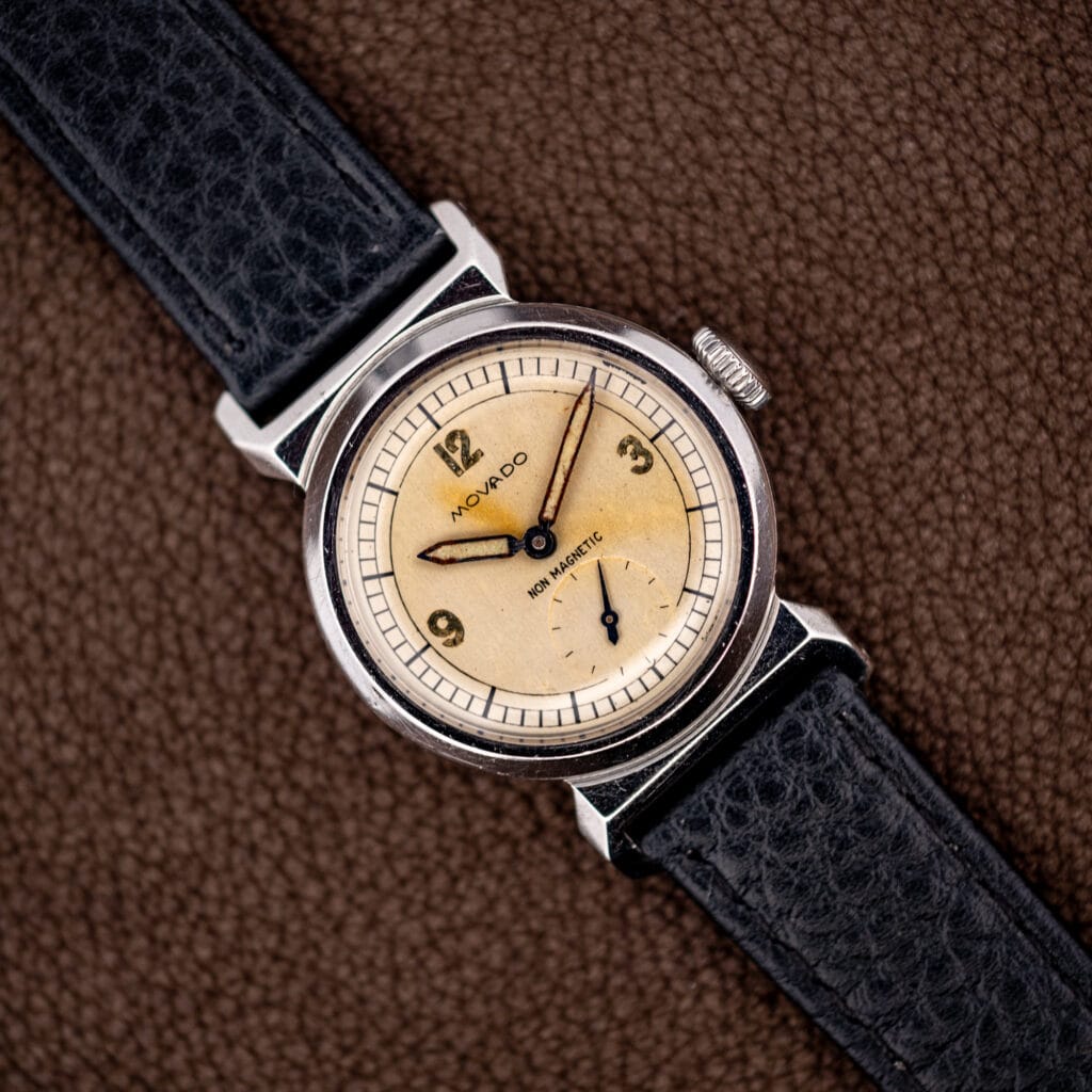 Vintage Movado Acvatic reference 11729 with aged cream dial and faceted scarab lugs on black leather.