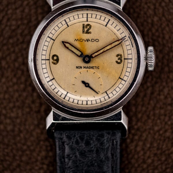 Aged eggshell Movado dial with gilt Arabic numerals at twelve, three and nine and warm patina.