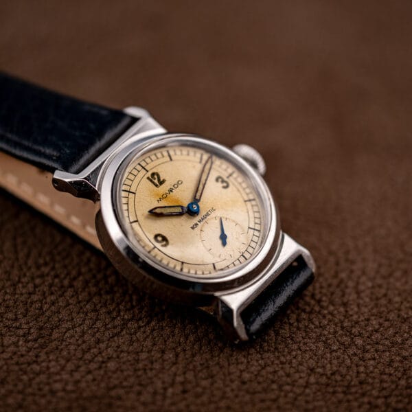 Movado cream dial with blued pencil hands and aged luminous plots.