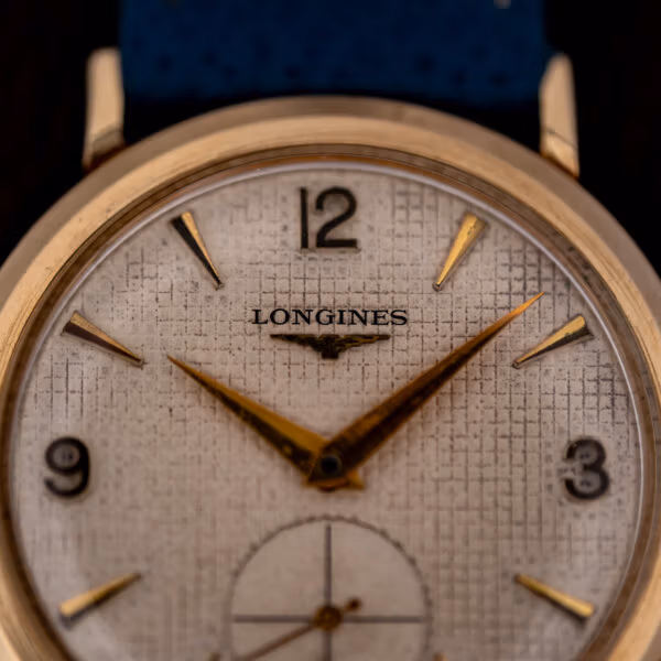 Longines Ref. 1044 dial macro showing fine woven waffle grid, applied gold batons and winged hourglass logo