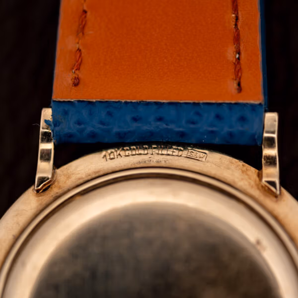 Longines 1044 case flank stamped 10K GOLD FILLED beside blue leather strap and faceted gold lug