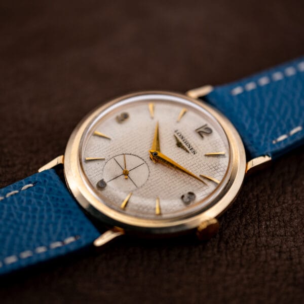 Longines 1044 waffle dial catching raking light across its ruled grid beside gold dauphine hands