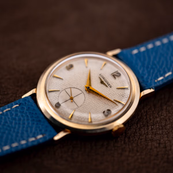 Longines 1044 waffle dial catching raking light across its ruled grid beside gold dauphine hands