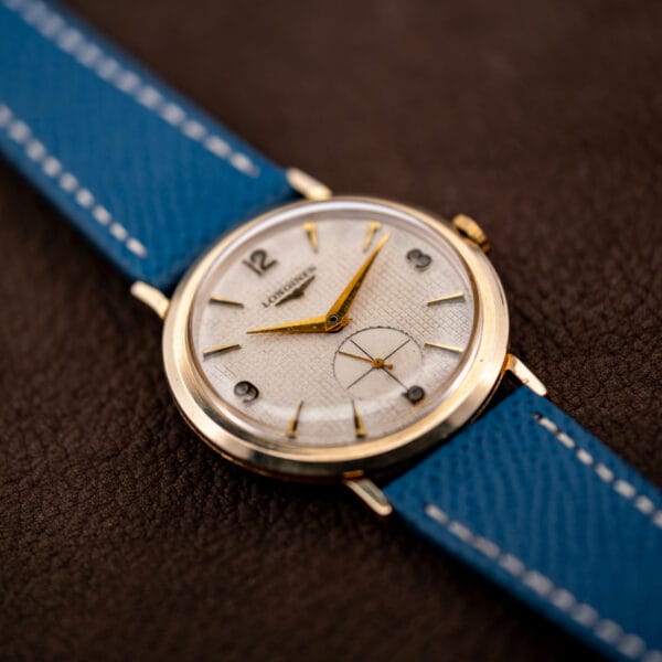Vintage Longines waffle dial 1044 on blue leather strap, gold filled case against brown leather