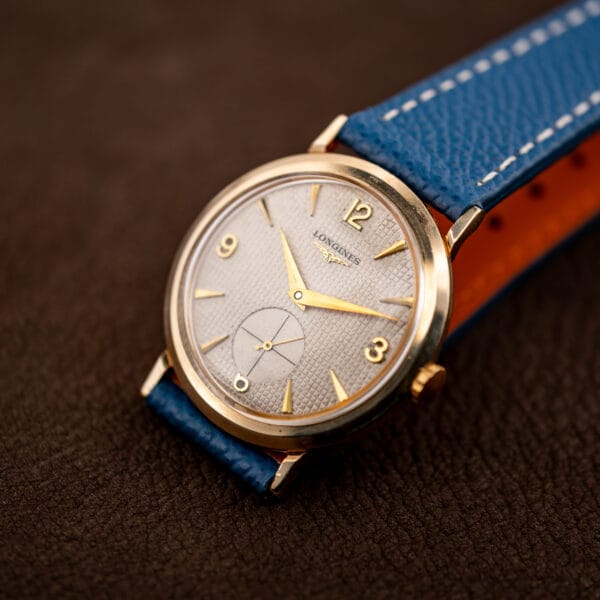 Longines Ref. 1044 upright on blue strap, waffle texture and applied gold indices under warm light