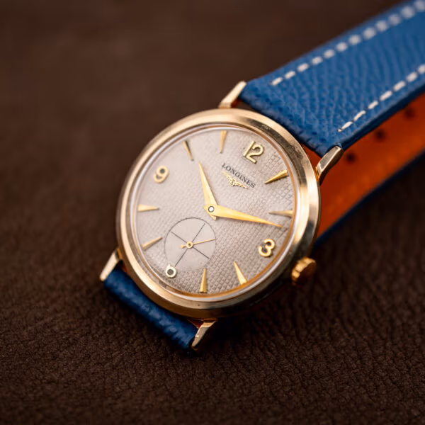 Longines Ref. 1044 upright on blue strap, waffle texture and applied gold indices under warm light