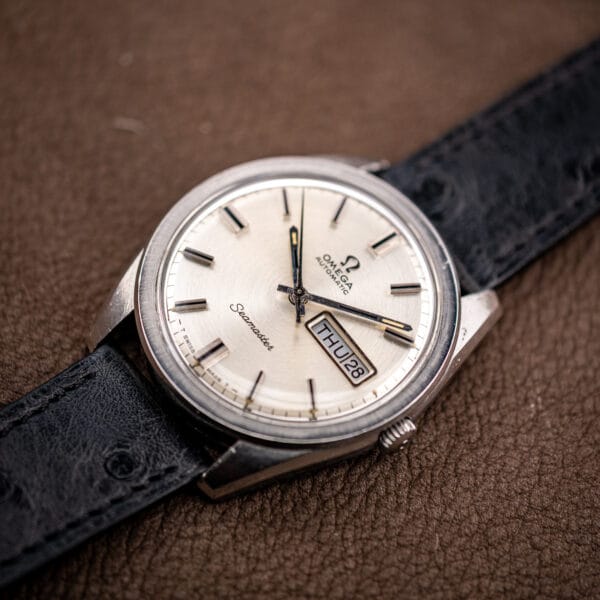 Vintage Omega Seamaster 166.032 day-date watch photographed at an angle across a brown leather surface