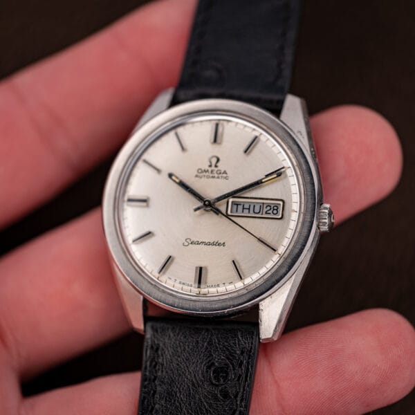 Vintage Omega Seamaster 166.032 held in hand, silver dial and day-date window facing the camera
