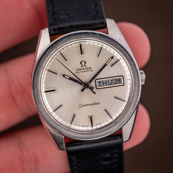 Omega Seamaster 166.032 in hand showing the silver dial, applied batons and day-date window at three