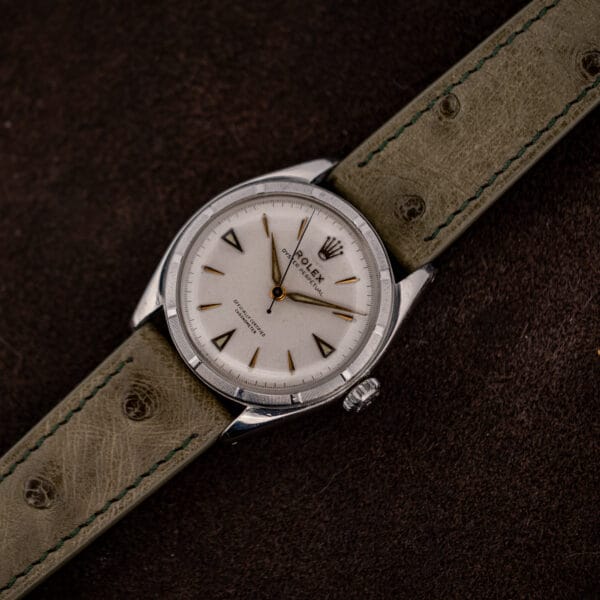 Angled overhead view of the Rolex 6085 on olive ostrich strap, engine turned bezel and fluted crown visible