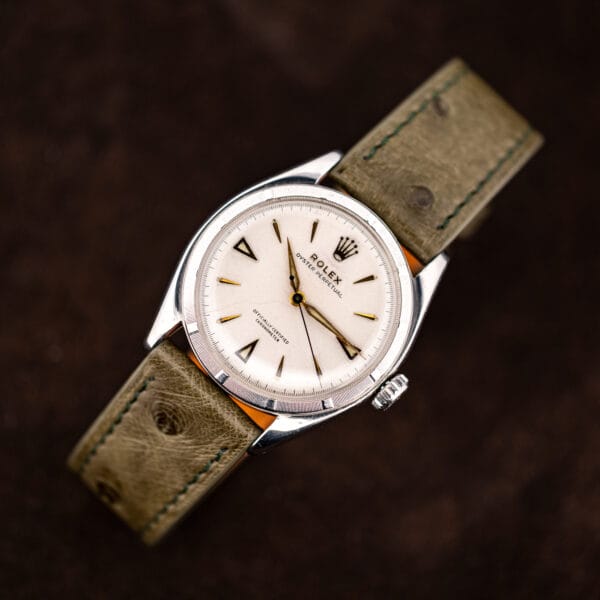 Rolex Oyster Perpetual 6085 angled on suede with dial text, drilled lugs and olive strap in frame