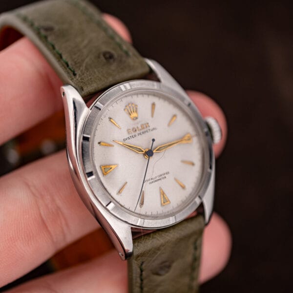 Rolex 6085 held in hand showing drilled lugs, domed crystal and the tan lined olive ostrich strap