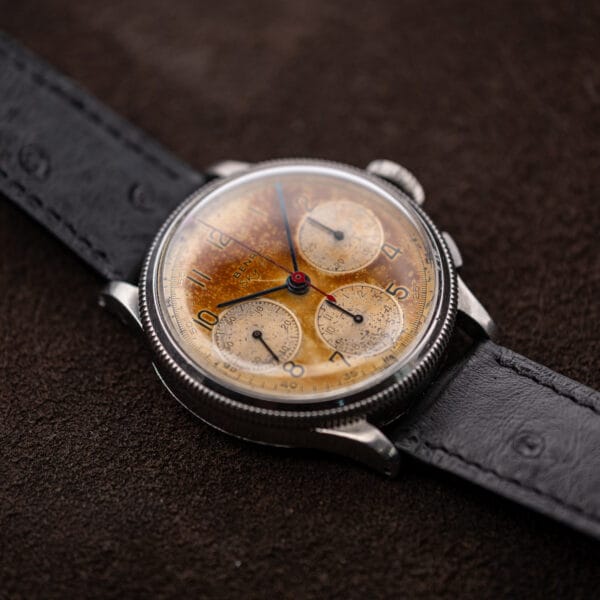 Benrus Sky Chief chronograph angled with the coin-edged bezel catching light on brown suede
