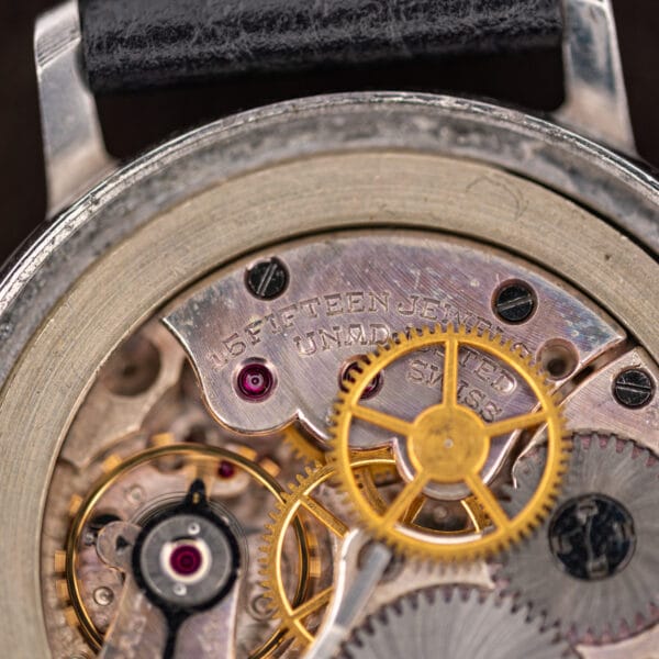 Macro of the Movado movement stamped 15 FIFTEEN JEWELS, UNADJUSTED and SWISS beside a large gilt wheel