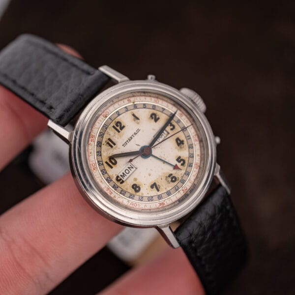 Movado 14819 in hand showing the blued date pointer with red arrow tip and darkened faceted hands